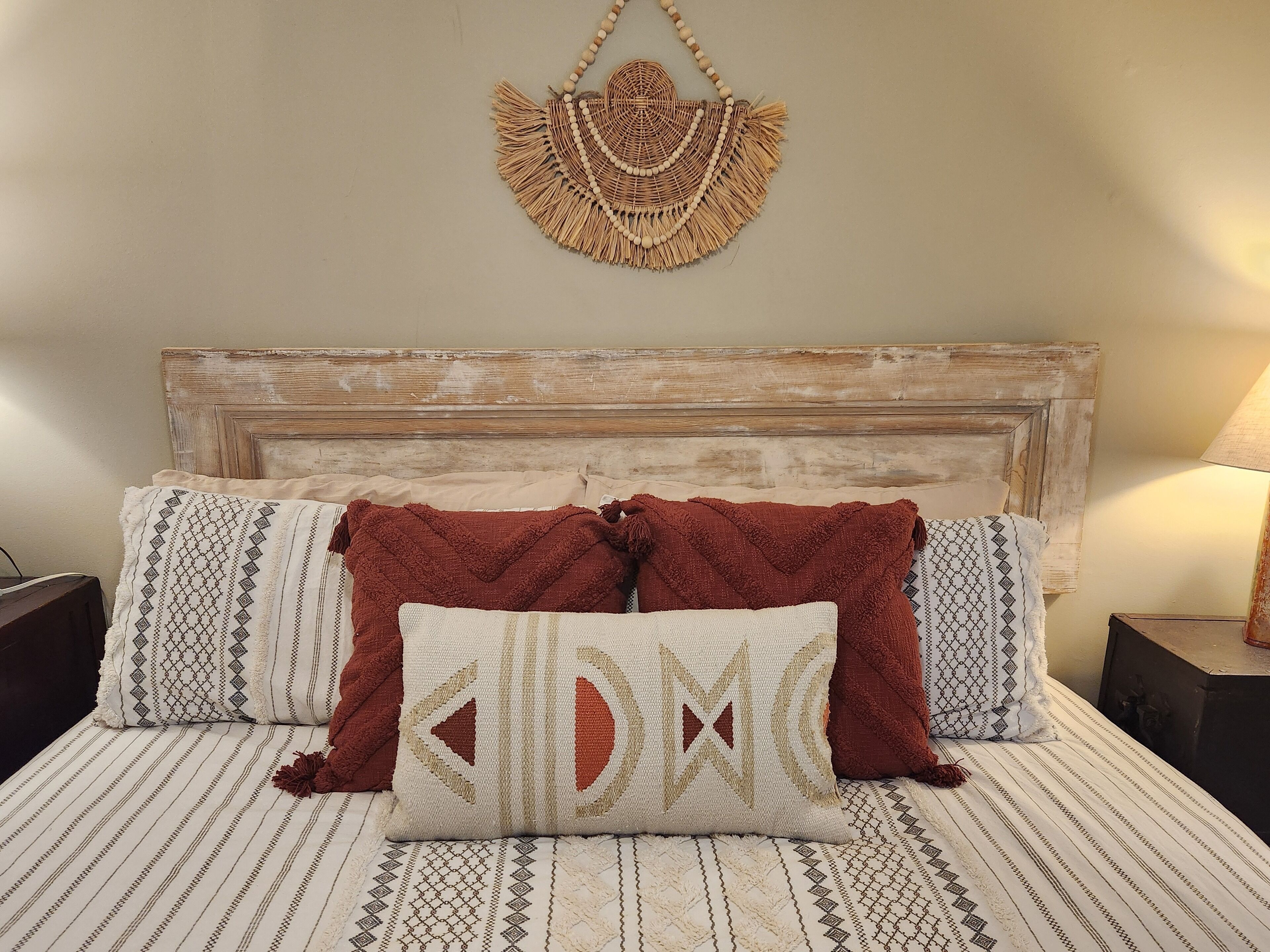 Un lit avec une literie à motifs, deux oreillers et une décoration murale en macramé.
