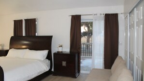 Un dormitorio con cama, mesita de noche, sofá y puerta corrediza de vidrio que da a un espacio exterior.