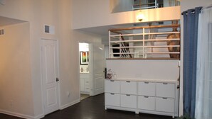 Un interior moderno con una escalera de madera, unidades de almacenamiento blancas y una mesa de vidrio con una planta.