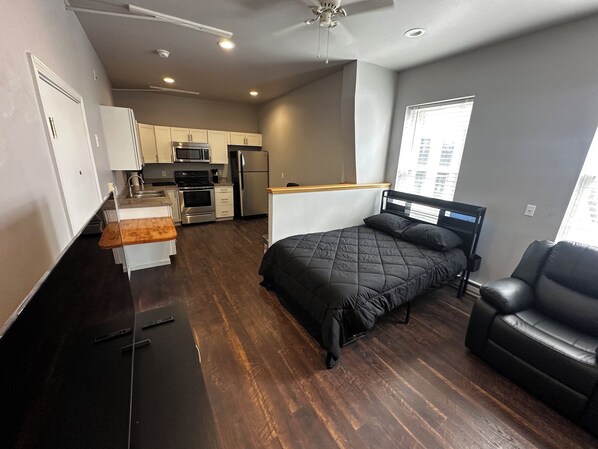 A compact living space with a kitchenette, a bed, a seating area, and a window with a view. - Studio on Main Street (Frostburg)