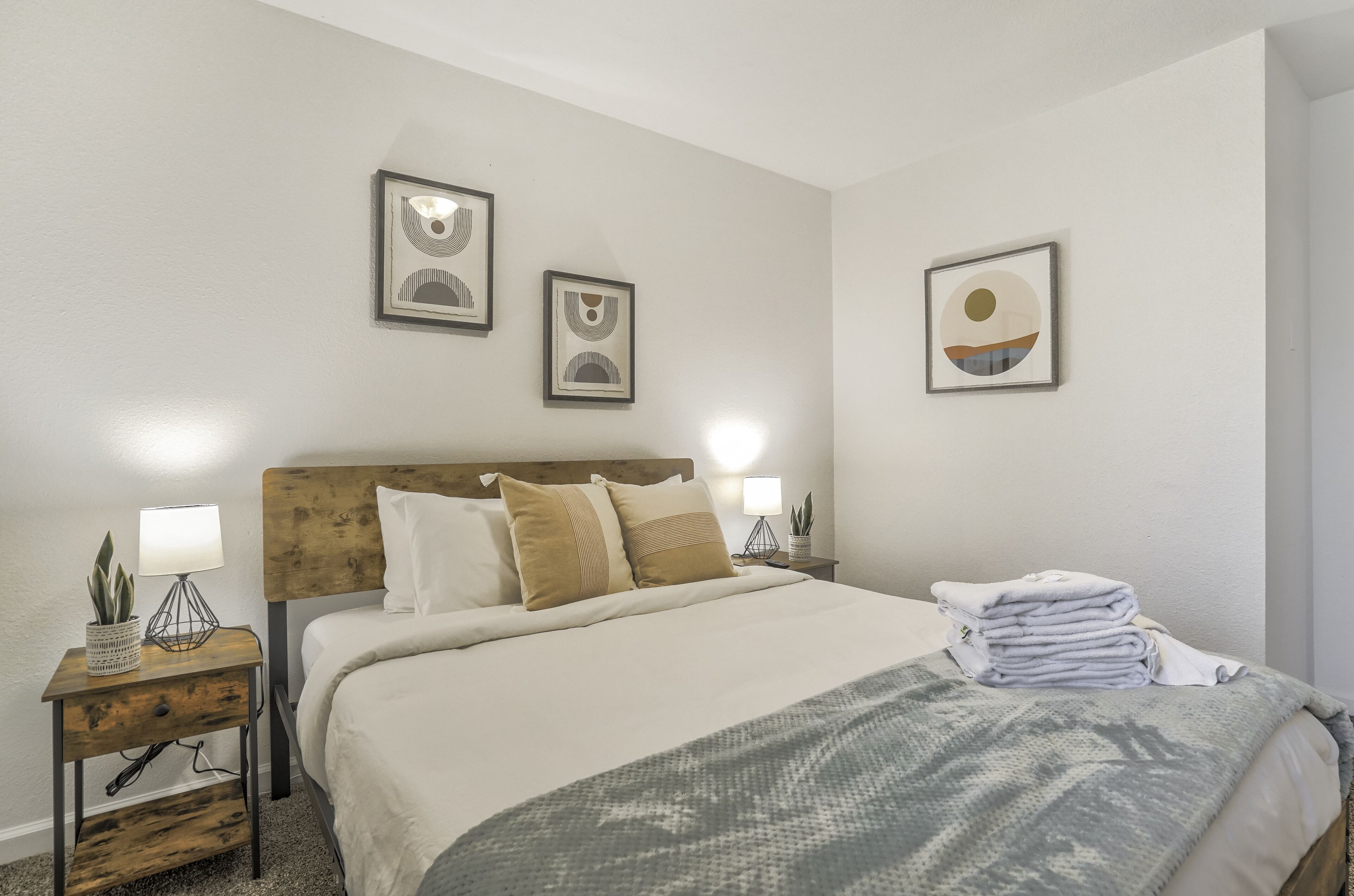 A neatly made bed with a wooden headboard, two bedside tables with lamps, and framed artwork on the wall.