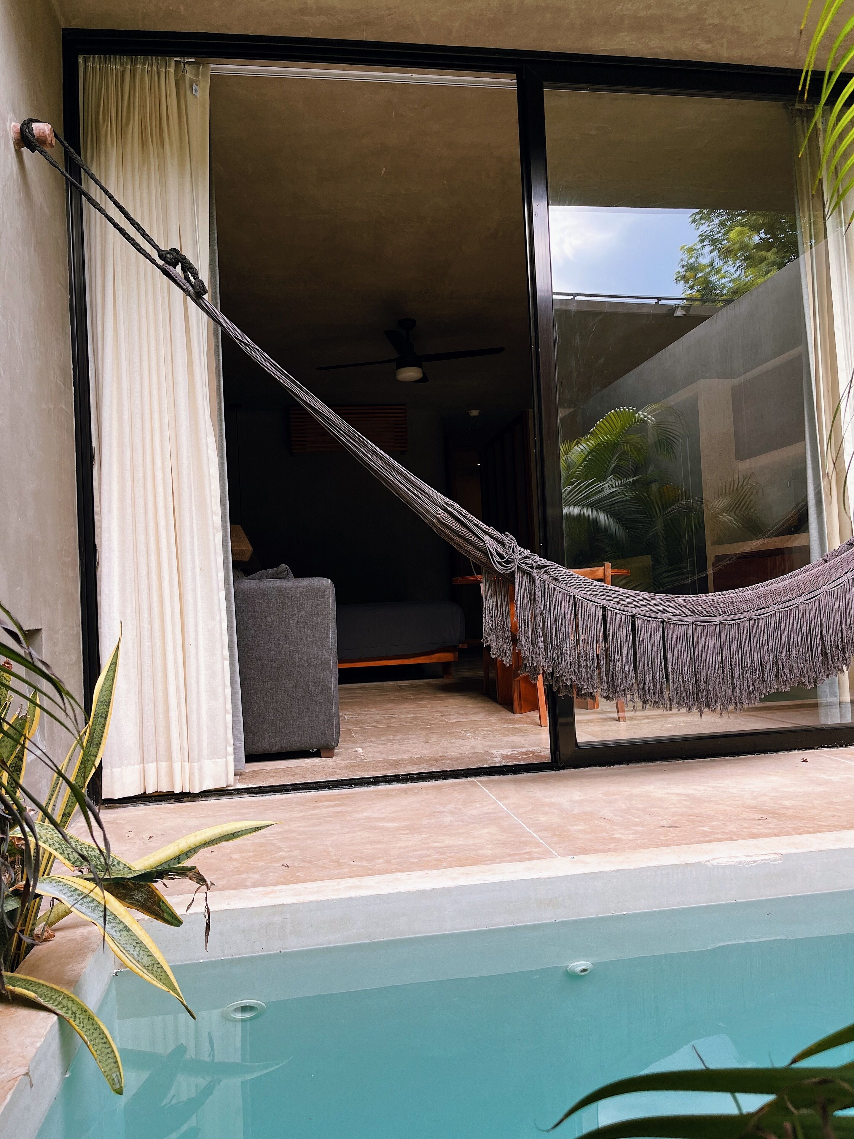A hammock over a poolside area with a sliding glass door leading to an interior space.