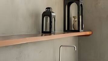 Una cucina con uno scaffale di legno, una macchina da caffè nera, un vaso bianco e un lavandino.