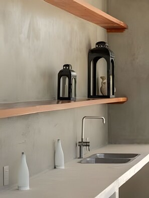 Eine Küche mit einem Holzboden, einer schwarzen Kaffeemaschine, einer weißen Vase und einem Spülbecken.