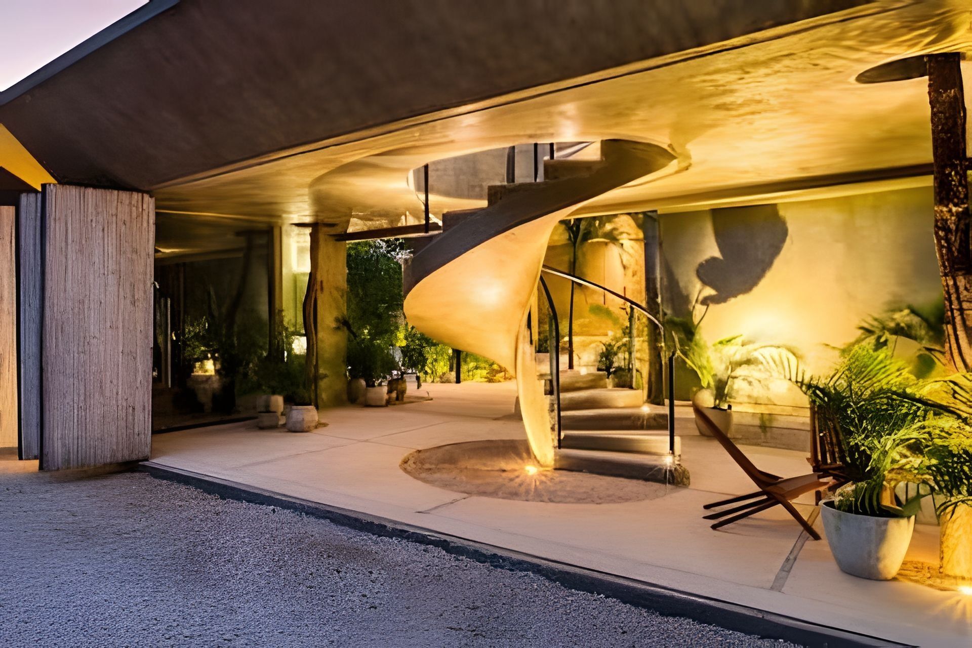 A modern building with a spiral staircase, outdoor seating, and potted plants.