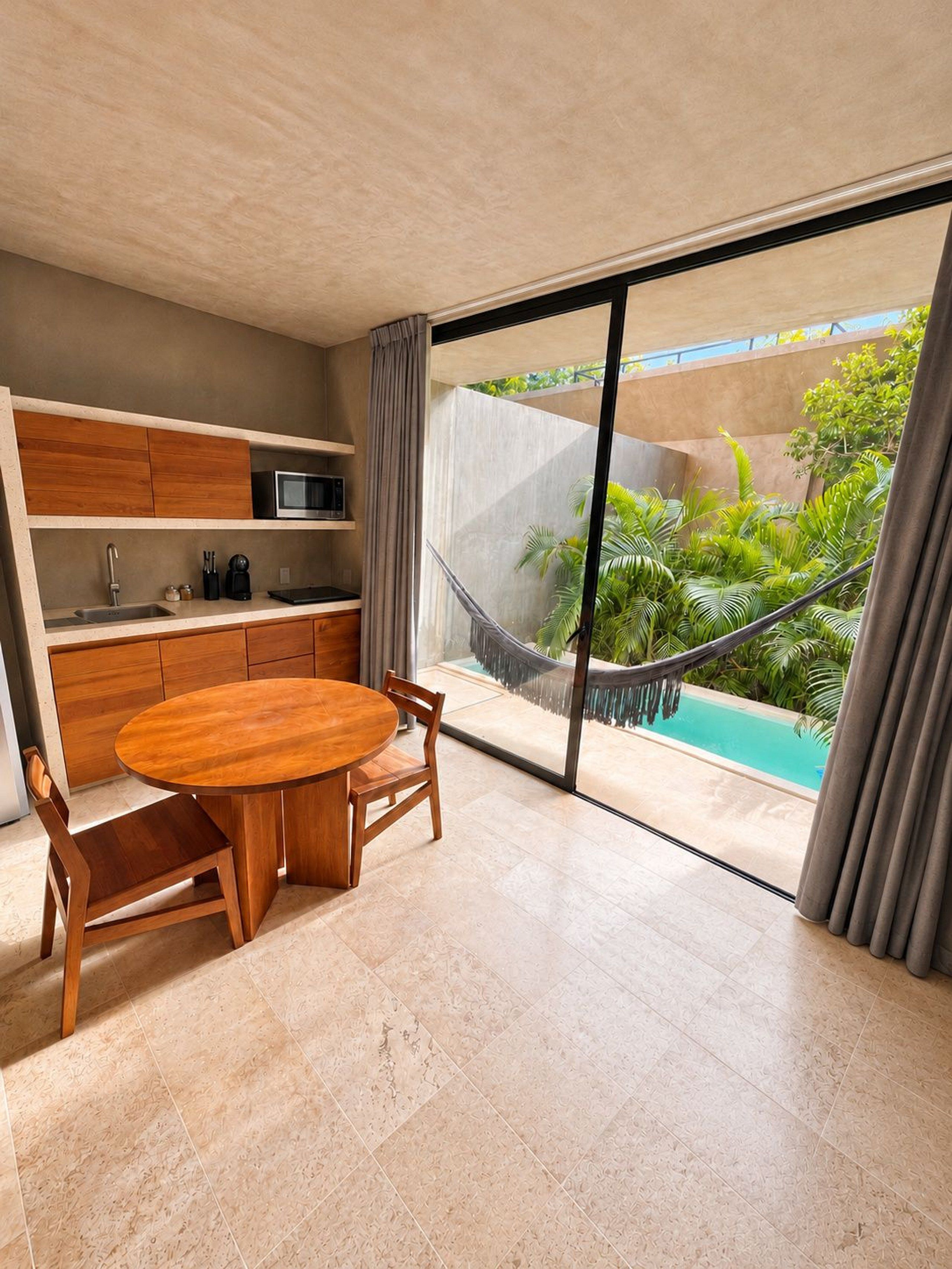 A modern kitchen with a round wooden table and chairs, a built-in microwave, and a view of a swimming pool through large windows.