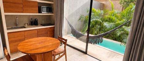 A modern kitchen with a round wooden table and chairs, a built-in microwave, and a view of a swimming pool through large windows.