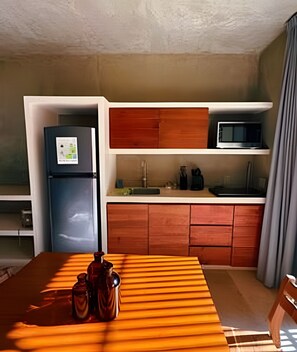 Een kleine keuken met een koelkast, magnetron en houten keukenkastjes.