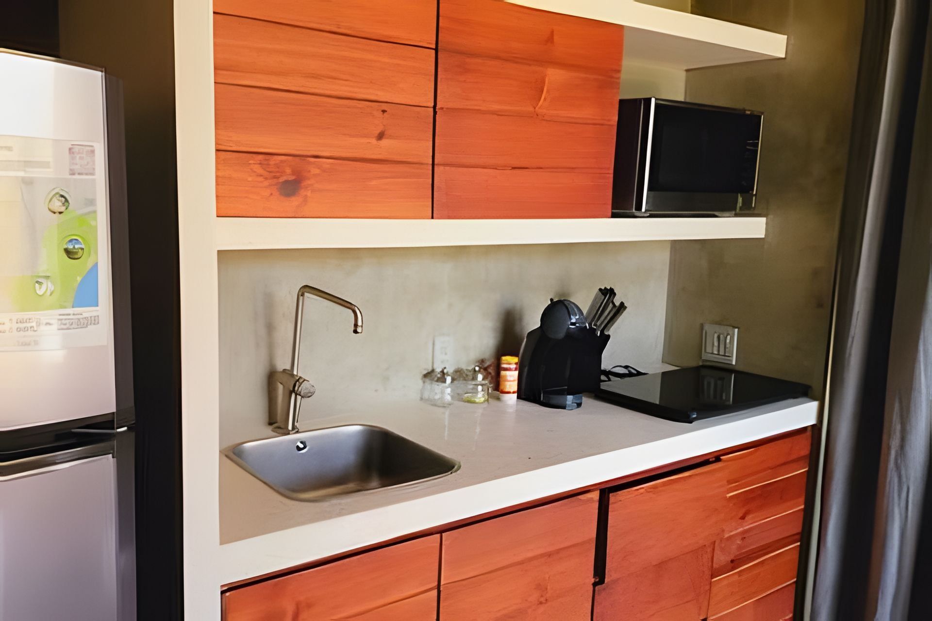 Eine Küche mit einer Edelstahl-Spüle, Holzschränken, einer schwarzen Mikrowelle und einem Kühlschrank.