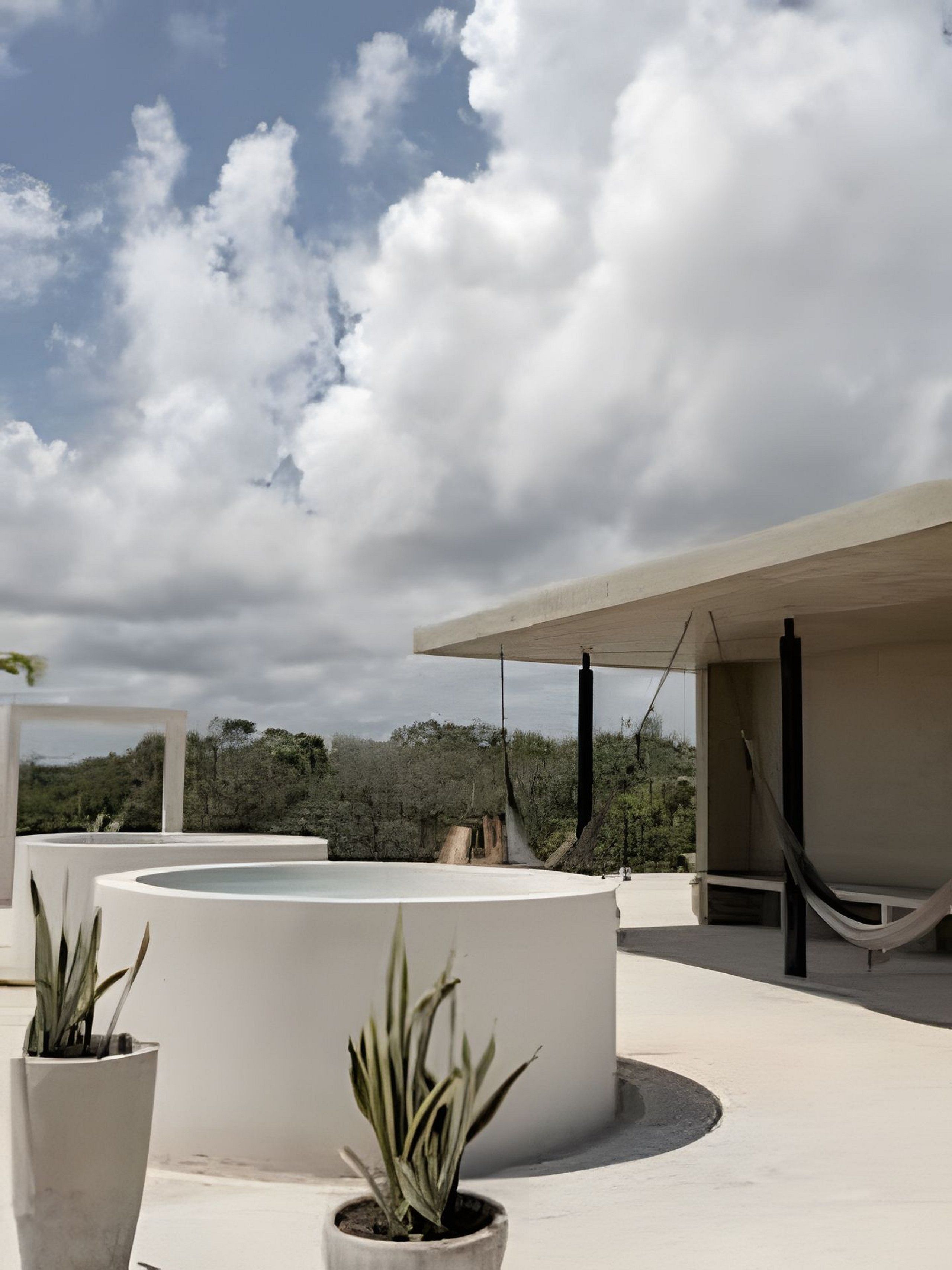 Eine Dachterrasse mit einer Hängematte, Topfpflanzen und Blick auf den Himmel und die Bäume.