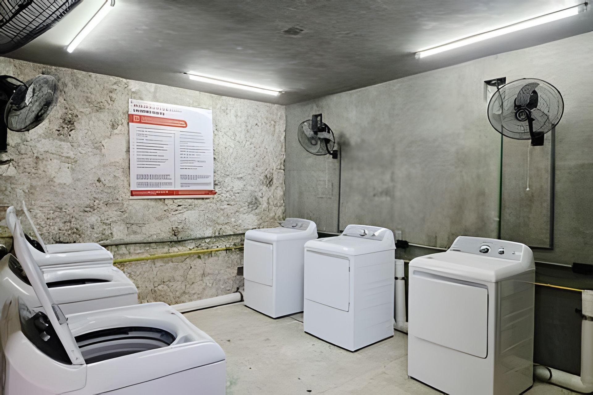 A laundry facility with three washing machines and two wall-mounted fans.