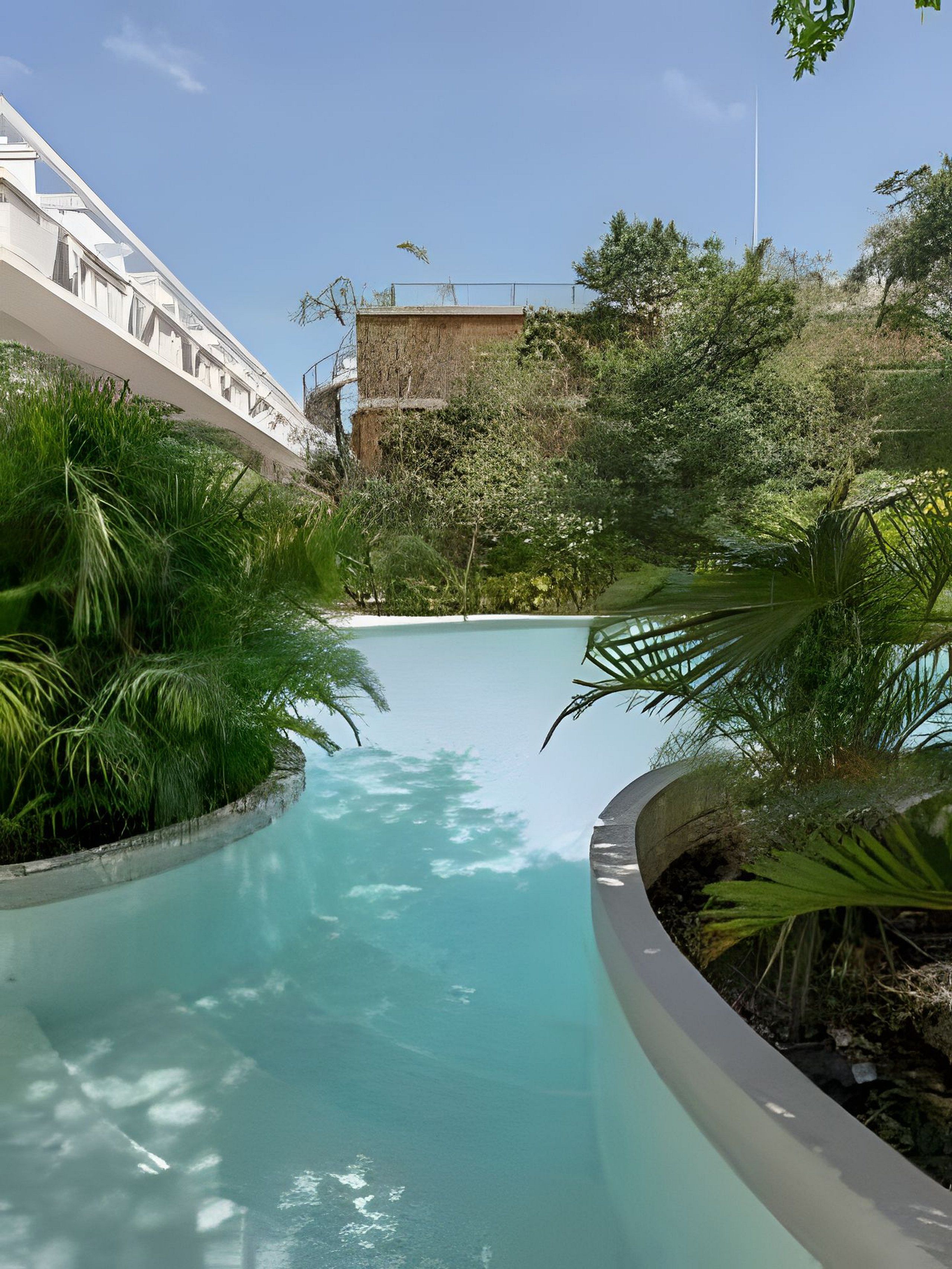A swimming pool with a curved edge, surrounded by lush greenery and a building in the background.