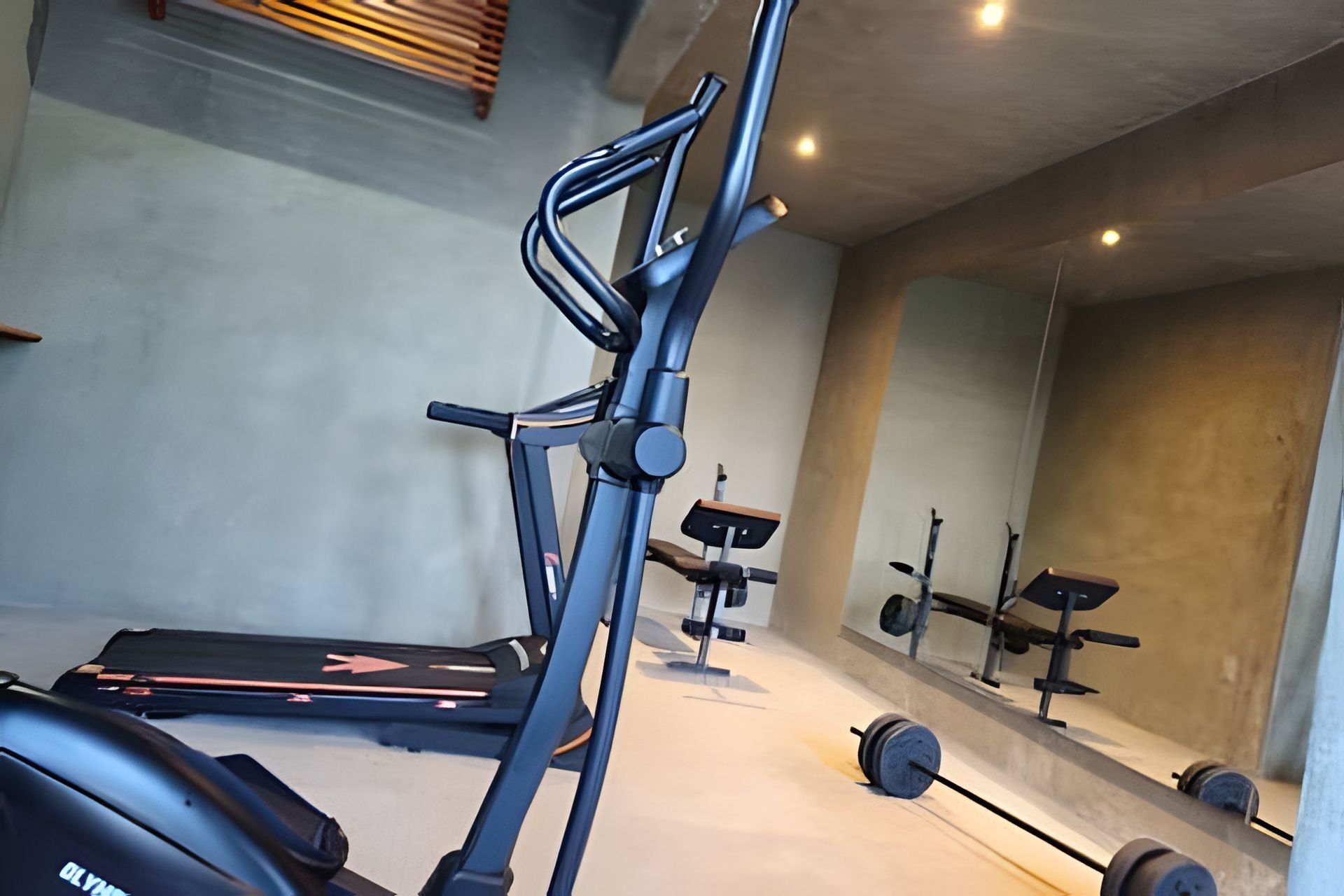 Ett gym med träningsutrustning, inklusive ett löpband, en viktbänk och hantlar.