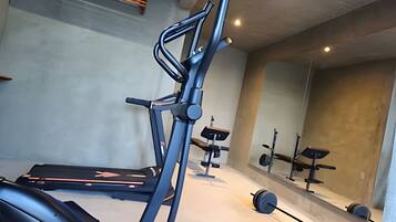 Ett gym med träningsutrustning, inklusive ett löpband, en viktbänk och hantlar.