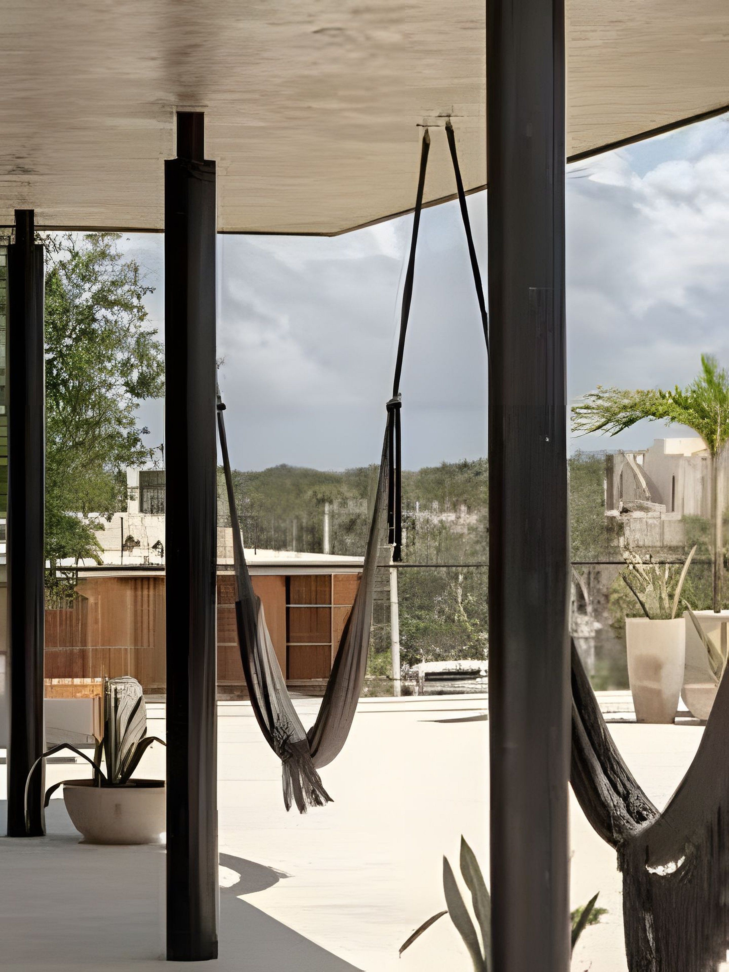 A hammock suspended between two poles in an outdoor area with potted plants and a view of a building in the background.