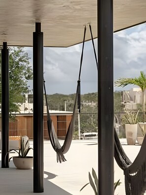 A hammock suspended between two poles in an outdoor area with potted plants and a view of a building in the background.