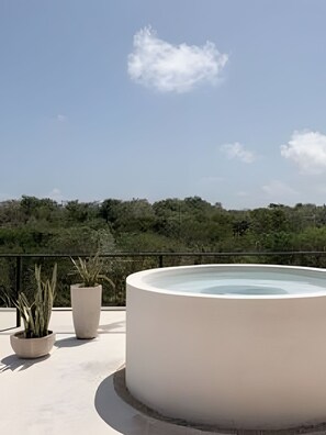 Une terrasse sur le toit dotée d’un jacuzzi circulaire, de plantes en pot et offrant une vue sur une colline boisée.