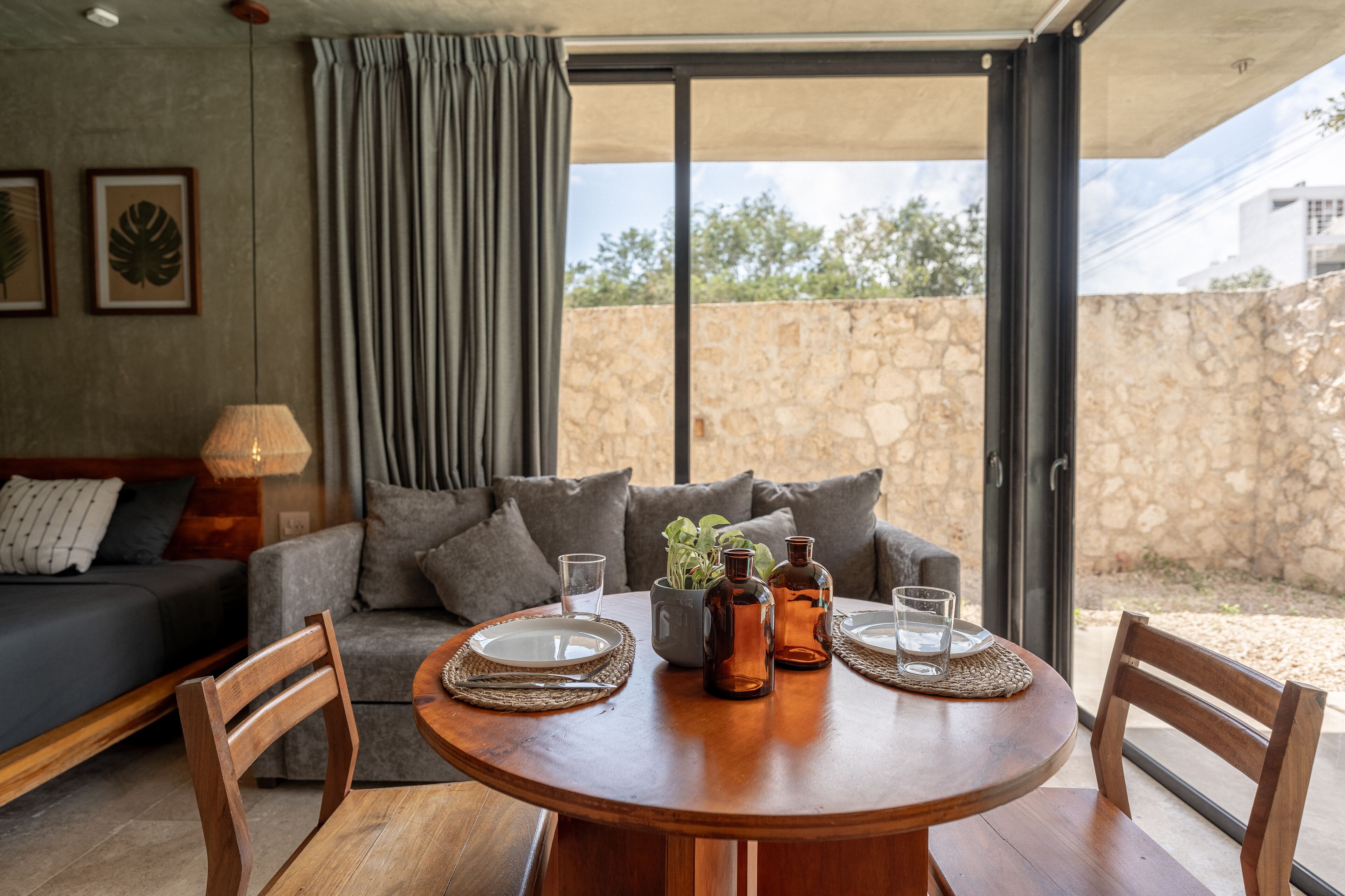 Un coin repas comprenant une table ronde en bois, deux chaises, un canapé et une fenêtre avec des rideaux.