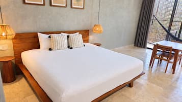 Una camera d'albergo con un letto grande, una testiera in legno, due lampade ai lati del letto, un tavolino e vista all'esterno attraverso una finestra con tende.