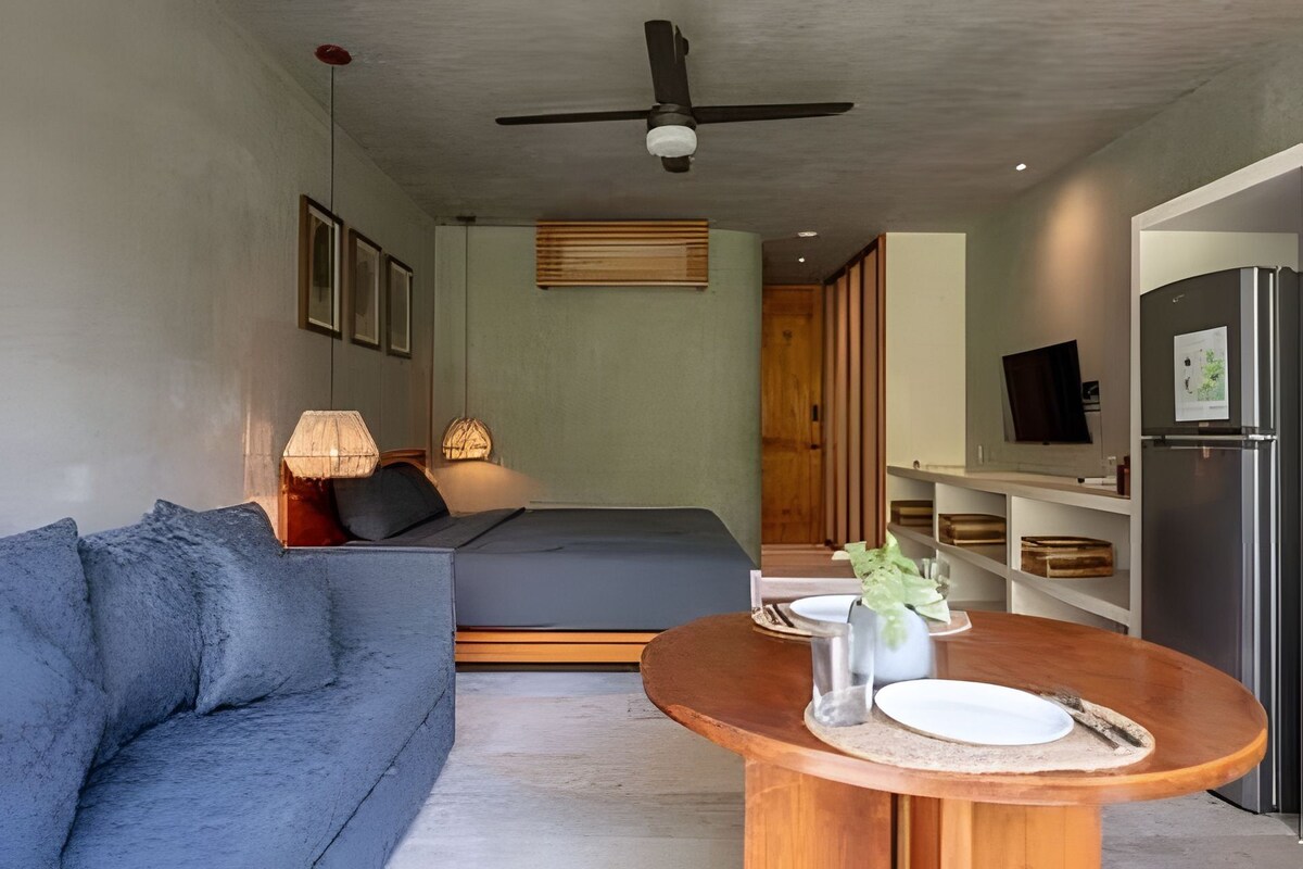 Un espace de vie moderne comprenant un canapé, une table à manger, un lit et un coin cuisine avec un réfrigérateur.