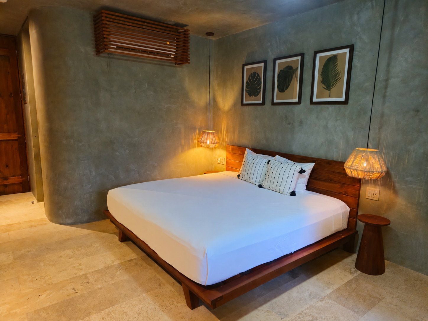 Un dormitorio con una cama grande, cabecera de madera, lámpara de noche y un cuadro con hojas en la pared.