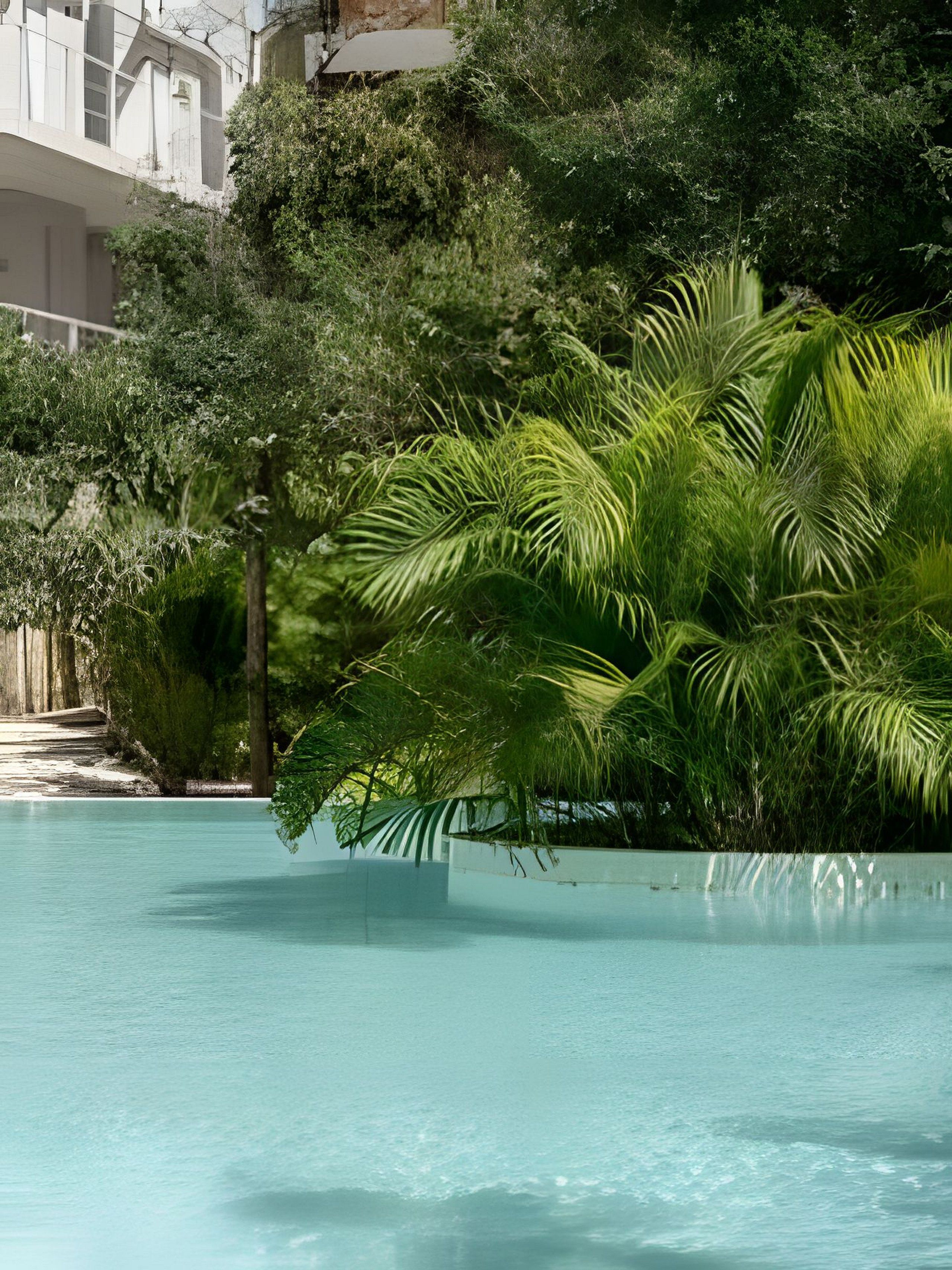 Une piscine entourée d’une végétation luxuriante et un bâtiment doté de balcons.