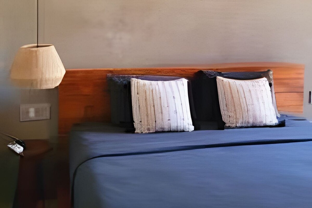 Une chambre d’hôtel avec un lit, une table de chevet, une lampe et trois œuvres d’art représentant des feuilles, encadrées et accrochées au mur.