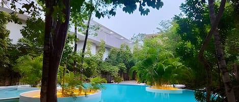 Piscina rodeada por árvores e um edifício com teto plano.