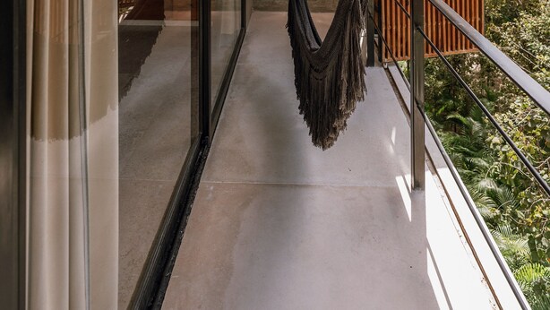 Een modern balkon met een hangmat, glazen deuren en uitzicht op groen.