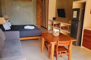 Een kleine kamer met een bed, een houten tafel en een kitchenette.