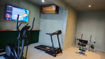 Ein Fitnessstudio mit Trainingsgeräten, darunter Laufband, Crosstrainer und Gewichte.
