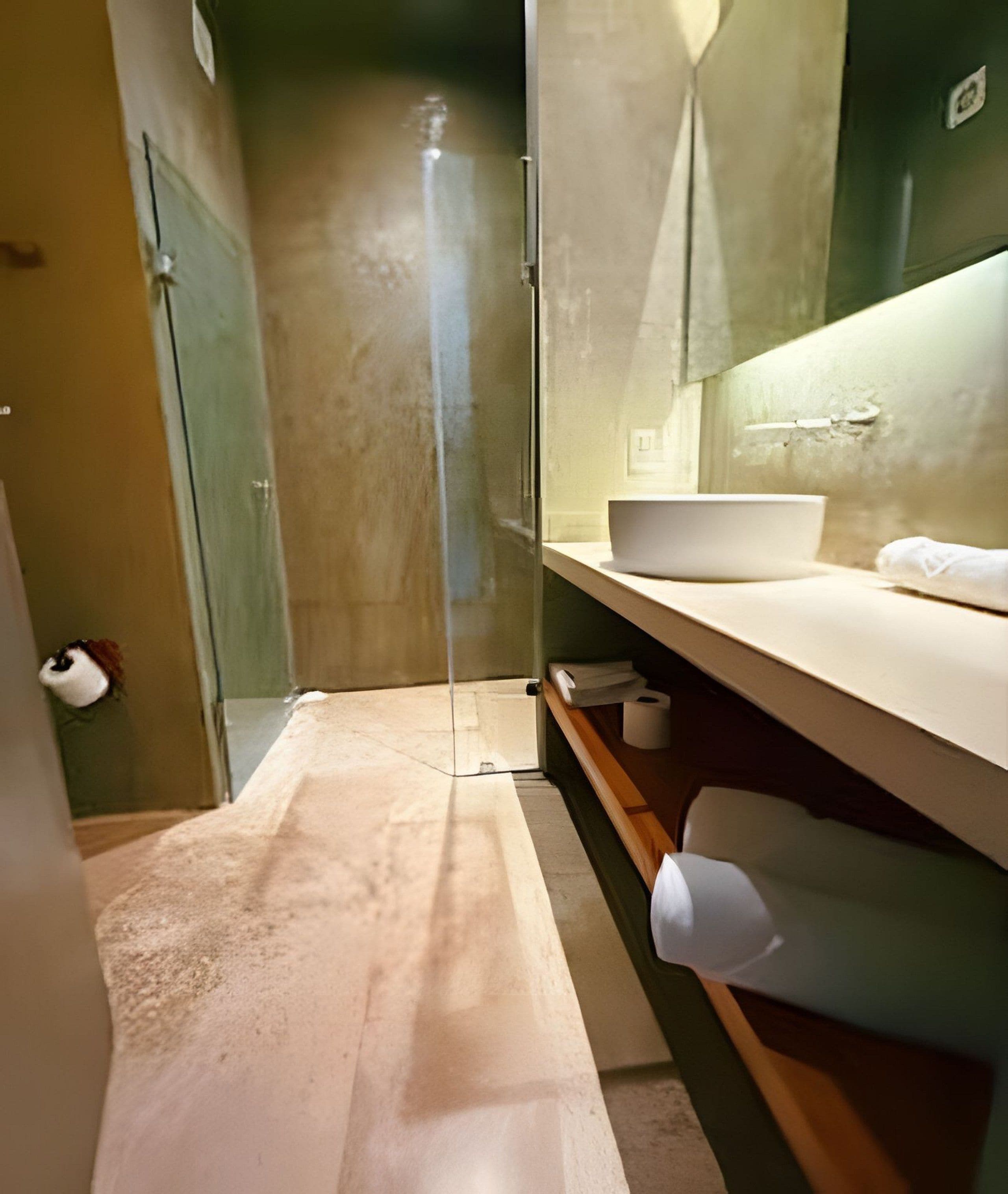 A narrow bathroom with a glass shower enclosure, a white sink, and a towel on the counter.