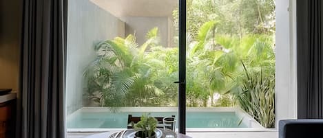 A dining area with a table, a potted plant, and a view of a swimming pool and lush greenery outside.
