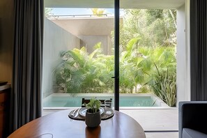 A dining area with a table, a potted plant, and a view of a swimming pool and lush greenery outside.