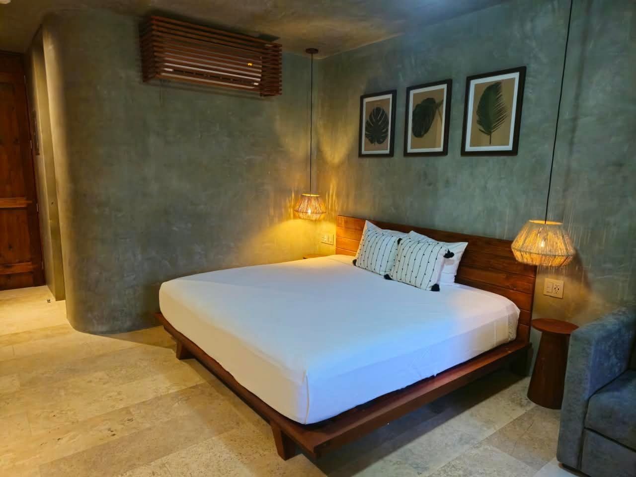 A bedroom with a large bed, two bedside lamps, and three framed leaf artworks on the wall.