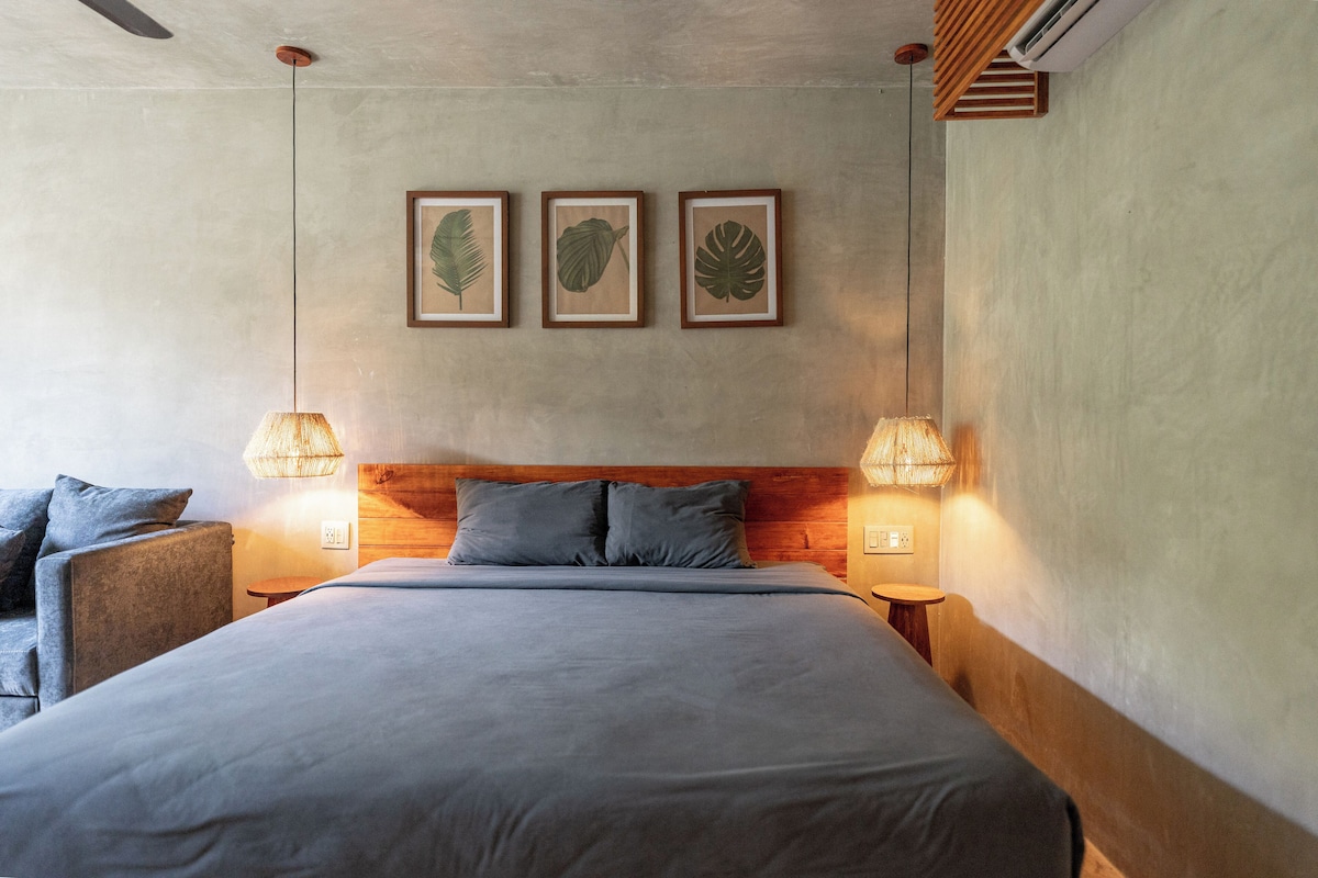 Un dormitorio con una cama grande, dos lámparas de noche, un cabecero de madera y tres hojas enmarcadas en la pared.