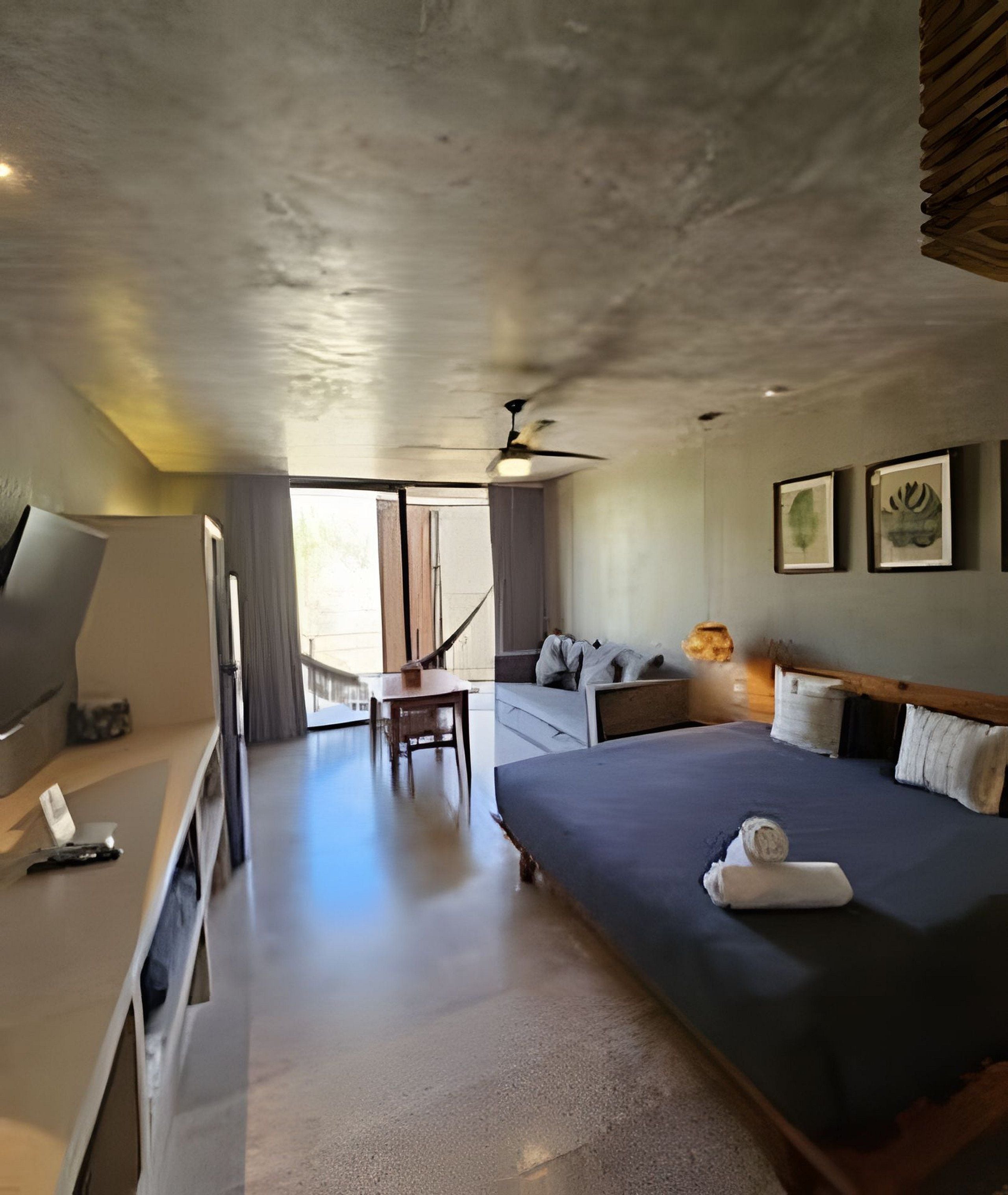 A hotel room with a bed, a desk, a chair, a television, and a ceiling fan.