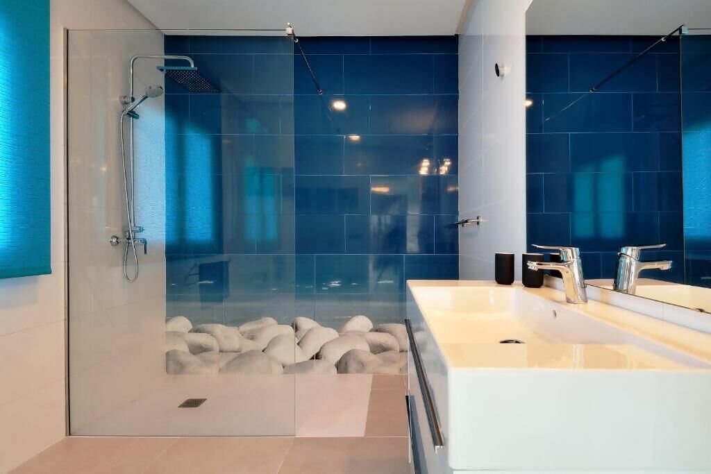 Un baño moderno con ducha de vidrio, dos lavamanos y un espejo grande.