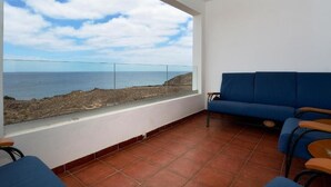 Un balcon avec vue sur la mer, un canapé bleu et un fauteuil.