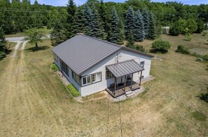A single-story house with a sloped roof, a covered porch, and a fenced yard. - Charming home in the heart of Northern Michigan's destinations and activities. (Cheboygan)