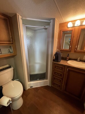 Een badkamer met een toilet, een douche met glasfolie, een wastafel en houten kastjes.