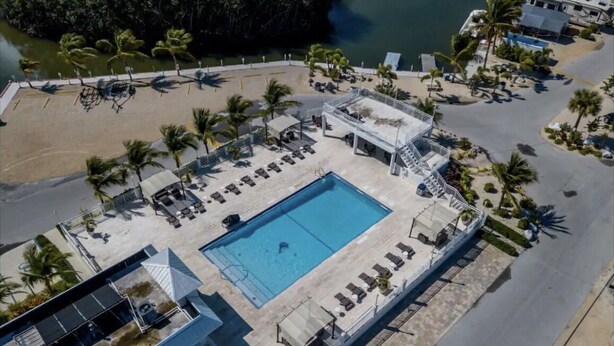 Vue aérienne d’un complexe hôtelier avec une piscine, des chaises longues et des palmiers.