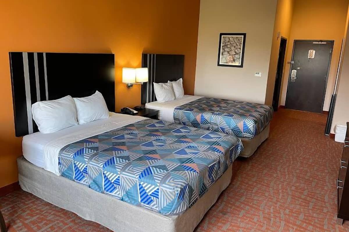 Ein Hotelzimmer mit zwei Betten, jeweils mit einem gemusterten Überwurf, einem Nachttisch mit Lampe und einem gerahmten Bild an der Wand.