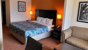 Una habitación de hotel con una cama, dos mesitas de noche, una silla y un sofá.