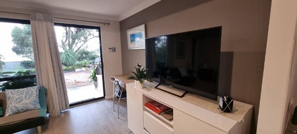 Ein Wohnzimmer mit einem großen Flachbildfernseher, einem Sofa, einem Couchtisch und einer Glasschiebetür, die zu einem Außenbereich führt.
