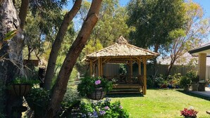 A gazebo in a garden with a lawn, trees, and potted plants. - Self Contained Granny Flat with Play Space (Alkimos)