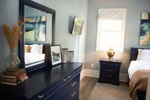 A bedroom with a bed, a dresser, a nightstand, a lamp, a mirror, and artwork on the walls.