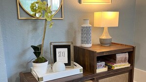 A wooden console table with a framed sign, a potted plant, a decorative vase, a lamp, and a shelf with books and board games. - Lovely Pet Frendly Home by Sherman (Boiling Springs)