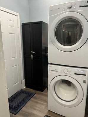 A laundry area with stacked washers and dryers, a black wardrobe, and a white door.