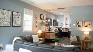 A modern living room with a grey leather sofa, a dining table, and a kitchen in the background. - Lovely Pet Frendly Home by Sherman (Boiling Springs)